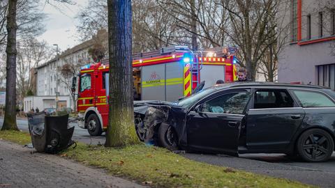 Ein Auto ist bei einem Unfall gegen einen Baum gekracht, dahinter steht ein Feuerwehrauto.