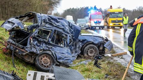 Völliges demolierter dunkler Pkw neben dem Fahrbahnrand, dahinter ADAC und Feuerwehr.