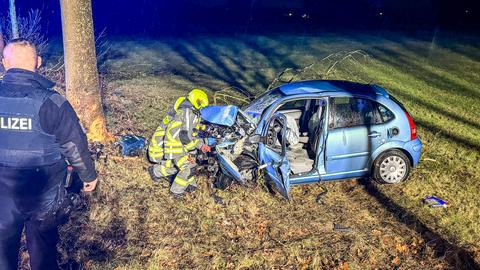 Feuerwehrleute an beschädigtem Auto auf einer Wiese neben einer Straße, Polizist steht daneben