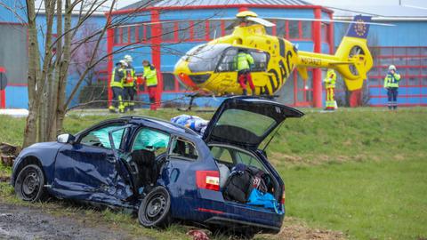 Ein Rettungshubschrauber landet auf einer Wiese, davor steht das beschädigte Auto der Familie.