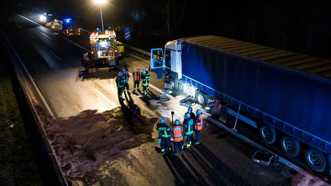 Ein Lkw steht nach einem Unfall auf einer Autobahn, daneben betrachten Feuerwehrleute eine Ölspur.