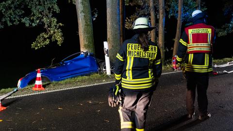 Einsatzkräfte an der Unfallstelle in Michelstadt - im Hintergrund ein blaues Auto an einem Baum.