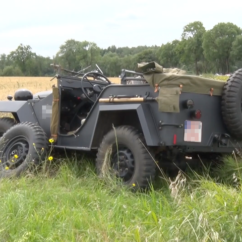 Ein Oldtimer-Allrad-Fahrzeug liegt neben der Straße, ein Reifen befindet sich neben dem Fahrzeug. Das Fahrzeug sieht aus wie ein alter Jeep - in dunkelgrau. 