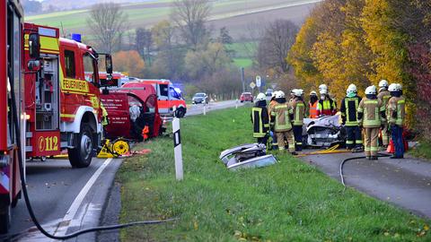 Feuerwehrautos und Rettungswagen stehen auf der Straße. Zahlreiche Feuerwehrleut stehen unweit davon auf einem Grünstreifen um ein demoliertes Auto.