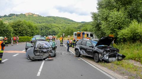 Zwei schwarze Autos stehen demoliert auf und an einer Straße, darum stehen Einsatzkräfte.