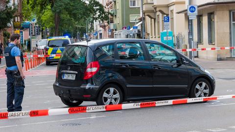 Ein schwarzes Auto steht nach einem Unfall hinter einem Absperrband, daneben ein Polizist.