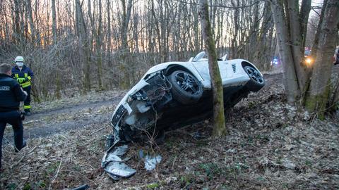 Ein Auto, das an der Front stark beschädigt ist, leht schräg an einem dünnen Baum neben einen Waldweg.