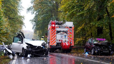 Zwei zerstörte Autos und ein Feuerwehrauto auf einer Straße.