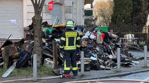 Ein Feuerwehrmann steht vor einem Berg verbrannter Gegenstände aus dem betroffenen Gebäude.