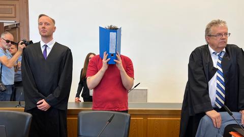 Angeklagter Jan P. steht im Verhandlungssaal des Landgerichts Gießen, er hält einen Aktenordner vor sein Gesicht