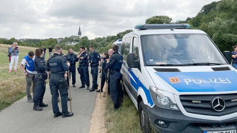 Viele Polizisten stehen im Kreis zum Gespräch neben einem Polizeiauto auf einem Feldweg. Im Hintergrund ein Dorf mit Kirchturm.