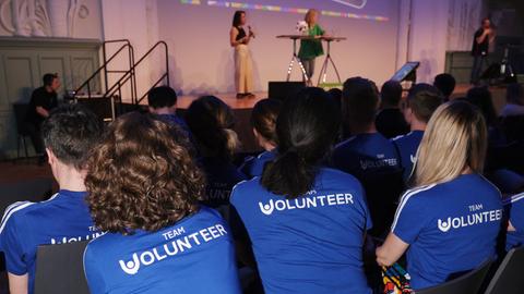 Menschen in einem Saal von hinten fotografiert - T-Shirt-Aufschrift Team Volunteer