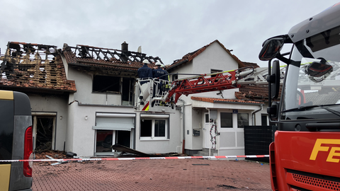 Ein Feuerwehrauto vor einem durch einen Brand zerstörten Wohnhaus.