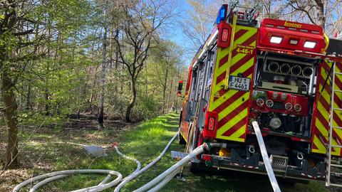 Ein Feuerwehrauto mit angeschlossenen Schläuchen steht an einem Waldrand.