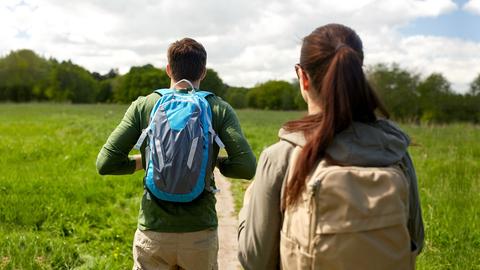 Junger Mann und junge Frau mit Rucksack von hinten beim wandern im Grünen