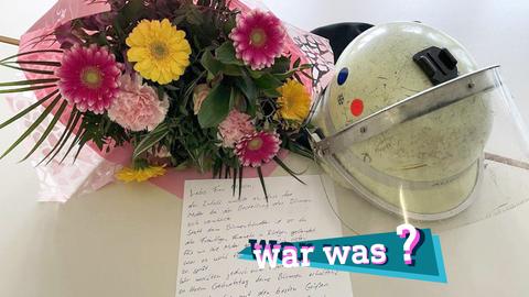 Foto von einem Blumenstrauß, einem Feuerwehrhelm und einem handschriftlichen Brief, die nebeneinander liegen. Auf dem Bild eine kleine, farbige Grafik mit dem Schriftzug "war was?".