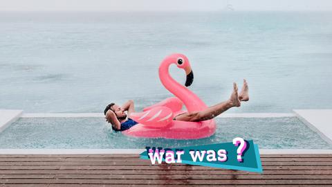 Foto eines Mannes, der in einem pinkfarbenen, aufgeblasenen Plastikschwan in einem Pool liegt und lächelnd den Regen auf sich niederprasseln lässt. Im Hintergrund das Meer. Auf dem Bild eine kleine, farbige Grafik mit dem Schriftzug "war was?".