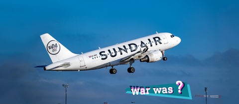 Ein Flugzeug mit der Aufschrift "Sundair" hebt ab. Im Hintergund blauer Himmel.  Auf dem Bild eine kleine, farbige Grafik mit dem Schriftzug "war was?".