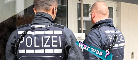 Foto von zwei Polizisten, die draußen vor einer Haustür stehen. Auf dem Bild eine kleine, farbige Grafik mit dem Schriftzug "war was?".