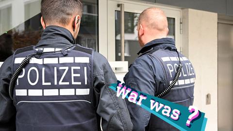 Foto von zwei Polizisten, die draußen vor einer Haustür stehen. Auf dem Bild eine kleine, farbige Grafik mit dem Schriftzug "war was?".