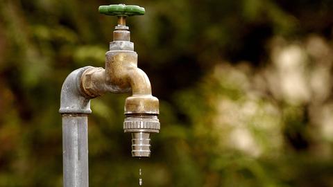 Wasser tropft aus einem Wasserhahn, im Hintergrund sieht man einen Garten