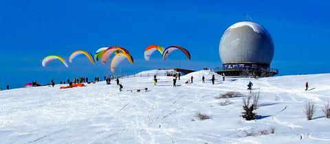 Gleitschirmflieger und Skifahrer auf den verschneiten Pisten an der Wasserkuppe