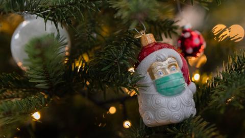 Ein Weihnachtsmann mit Coronamaske hängt als Schmuck in einem Weihnachtsbaum neben den traditionellen Weihnachtskugeln.