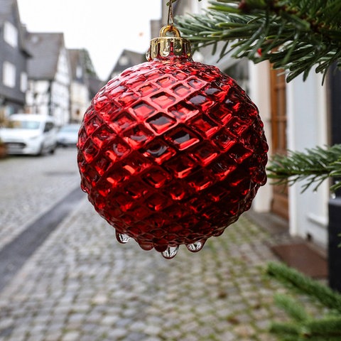 Rote Christbaumkugel groß im Bildvordergrund, dahiner Blick in eine Straße mit Fachwerkhäusern.