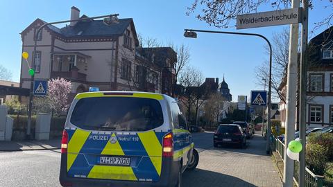 Polizeibus von hinten auf einem Bürgersteig, Schild "Walderbachschule", Luftballons (weiß und grün) am Mast des Schildes