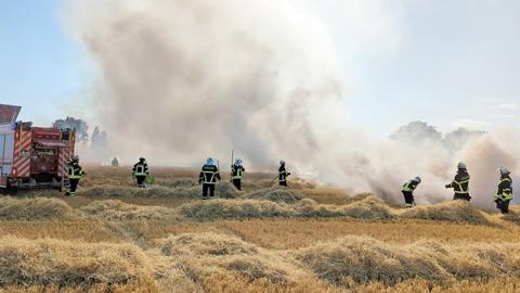 Feuerwehrleute auf einem Getreidefeld im Einsatz. Daneben ein Löschfahrezeug. Darüber voluminöse Rauchwolken.