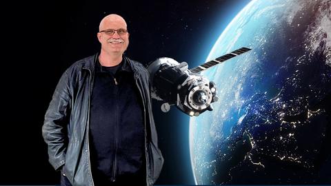 Ein Mann steht vor einem Weltraumfoto, auf welchem man die Erde angeschnitten sieht und daneben einen schwebenden Satelliten.