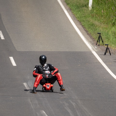 Der neue Weltrekordhalter sitzt auf einem gewöhnlichen roten Bobbycar, rechts auf einer Tafel werden 106 km/h angezeigt.