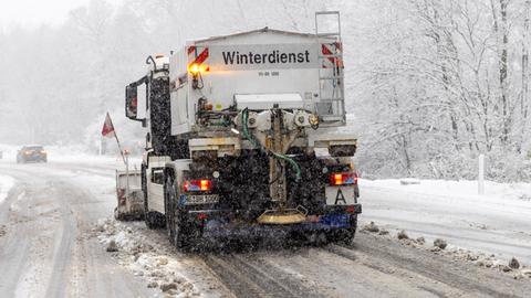 Ein Räumfahrzeug des Winterdienstes fährt auf einer verschneiten Straße entlang.