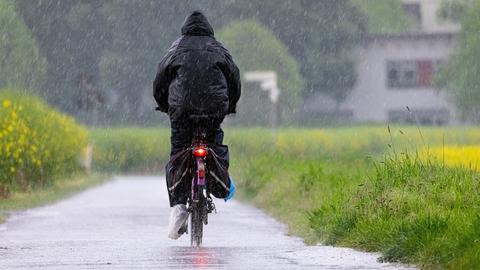 Ein Fahrradfahrer fährt bei starkem Regen einen Feldweg im Nordwesten von Frankfurt entlang