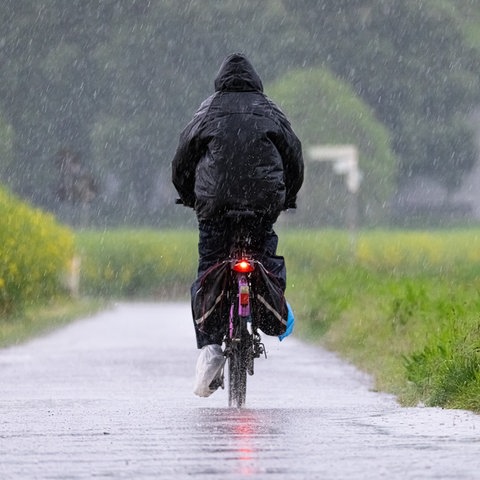 Ein Fahrradfahrer fährt bei starkem Regen einen Feldweg im Nordwesten von Frankfurt entlang