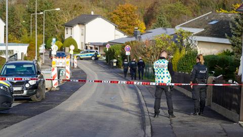 Blick in eine Straße eines Wohngebietes. Im Vordergrund ein Absperrband, hinter dem Absperrband Mitarbeitende der Polzei.