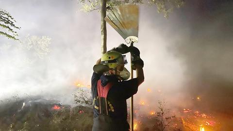 Eine Einsatzkraft der Feuerwehr mit einem Hilfsinstrument vor einem Feld voller Glut.