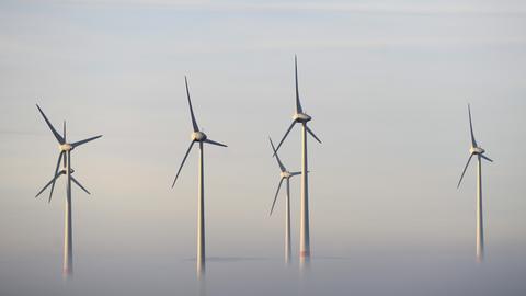 Windräder ragen aus Wolken und Nebel heraus.