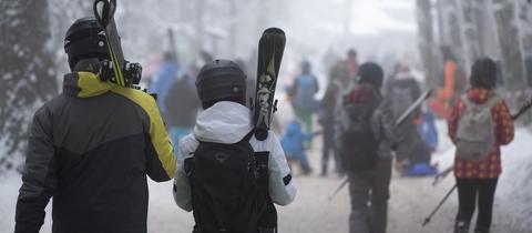 Menschen mit geschulterten Skiern auf einem verschneiten Waldweg an der Wasserkuppe.