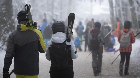 Menschen mit geschulterten Skiern auf einem verschneiten Waldweg an der Wasserkuppe.