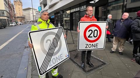 Ein städtischer Mitarbeiter und Verkehrsdezernent Wolfgang Siefert (Grüne) halten jeweils ein Tempo-20-Schild und ein Tempo-20-beendet-Schild in der Hand.