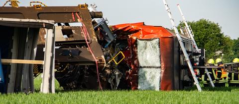 Eine Lok liegt neben den Gleisen auf einem Feld, Feuerwehr und Polizei stehen daneben.