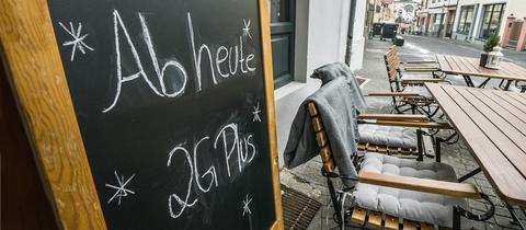 Auf einer Tafel im Außenbereich eines gastronomischen Betriebes steht "Ab heute nur noch 2 G Plus" geschrieben.