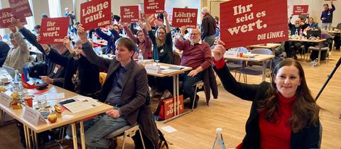 Bundesparteivorsitzende Janine Wissler, Landesvorsitzender Jan Schalauske und weitere Linken-Politikerinnen und -Politiker beim Parteitag halten Schilder mit politischen Forderungen hoch.