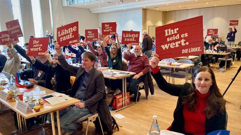 Bundesparteivorsitzende Janine Wissler, Landesvorsitzender Jan Schalauske und weitere Linken-Politikerinnen und -Politiker beim Parteitag halten Schilder mit politischen Forderungen hoch.