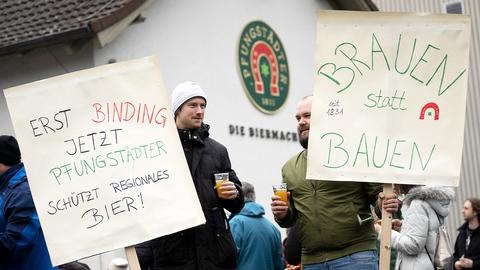 Zwei jungen Männer stehen mit Schildern, auf denen «Erst Binding jetzt Pfungstädter schützt regionales Bier!» und «Brauen statt Bauen» steht.