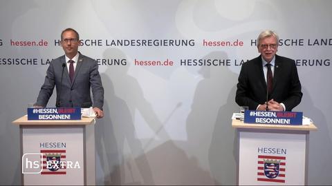 Gesundheitsminister Kai Klose und Ministerpräsident Volker Bouffier) stehen nebeneinander an Stehpulten. Im Hintergrund eine Wand mit den Schriftzügen und Logos der hessischen Landesregierung. 