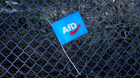 Ein blaues AfD-Fähnchen hängt in einem Maschendrahtzaun .