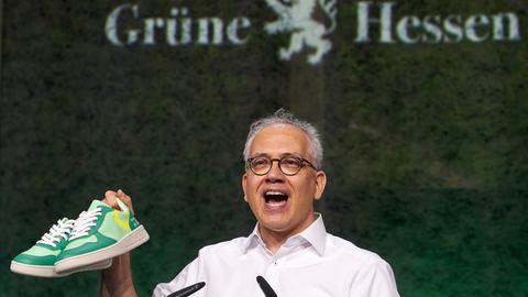 Tarek Al-Wazir mit grünen Turnschuhen in der Hand auf dem Landesparteitag der Grünen