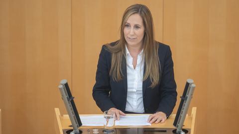 Eine Frau in weißer Bluse und schwarzem Blazer steht an einem Rednerpult mit der Aufschrift "Hessischer Landtag".